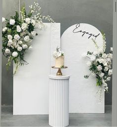 a wedding cake sitting on top of a pedestal next to white flowers and greenery