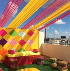 an outdoor area decorated with bright colored fabric and poufles on the roof top