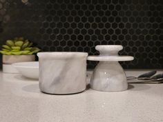 two marble salt and pepper shakers sitting on a counter next to a plate with utensils