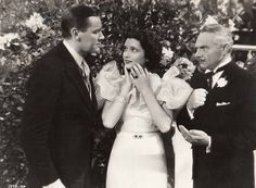 two men and a woman standing next to each other in front of a bush with flowers