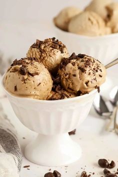 three scoops of ice cream in a white bowl with chocolate chips on the side