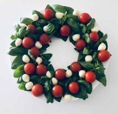 a white plate topped with a wreath made of tomatoes and basil leaves on top of it