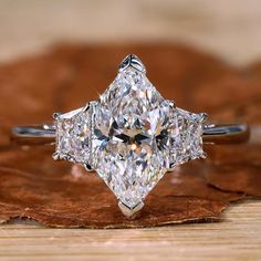 a three stone diamond ring sitting on top of a wooden table next to a leaf