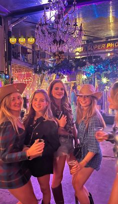 four women are posing for a photo in front of a store with lights and chandeliers