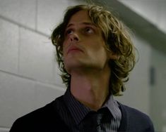 a man with curly hair wearing a vest and tie looking up at the sky while standing in front of a white brick wall