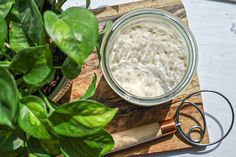 a jar of cream sitting on top of a wooden cutting board next to a potted plant