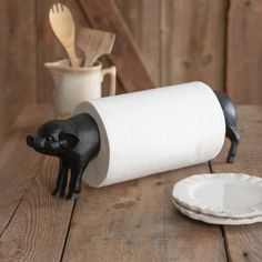 a black pig figurine next to a roll of toilet paper on a wooden table