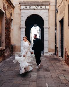 a man and woman are walking down the street in front of an archway holding hands