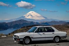 a white car parked in front of a mountain with snow on it's top