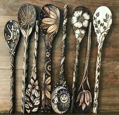 six spoons are lined up on a wooden surface with designs painted on the handles