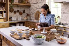 a woman standing in a kitchen preparing food on top of a wooden cutting board next to a counter