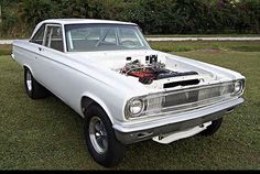 an old white car parked in the grass with its hood up and engine on it's side