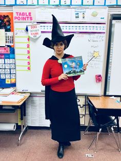 a woman in a witches hat holding a book while standing in front of a whiteboard