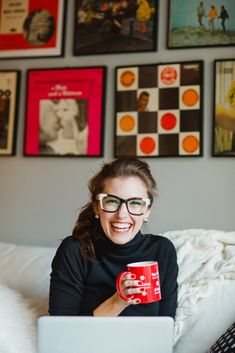 a woman sitting on a bed holding a red coffee mug and looking at the camera