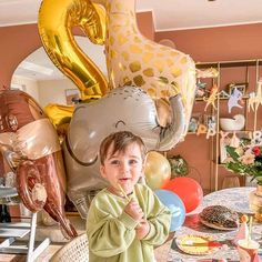 a little boy standing in front of a table with some balloons on it and an elephant balloon