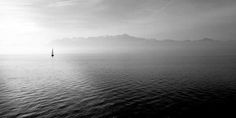 a sailboat in the middle of an ocean on a foggy day with mountains in the background