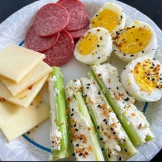 a white plate topped with meat, cheese and veggies next to hard boiled eggs