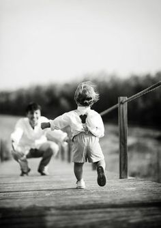 a little boy running across a wooden bridge next to a man in white shirt and tie