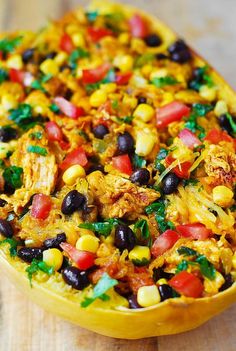 a yellow dish filled with chicken, black beans and veggies on top of a wooden table