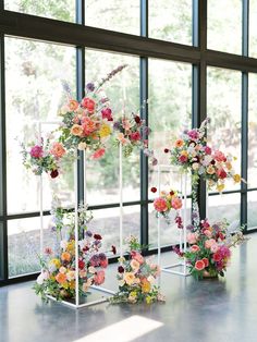 an assortment of flowers are displayed in front of large windows