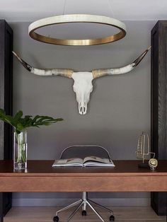 a cow skull mounted to the side of a wall above a wooden desk with an open book on it