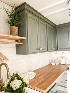 a kitchen with green cabinets and wooden counter tops, white appliances and flowers on the counters