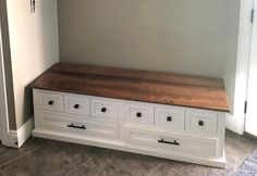 an empty room with white drawers and a wooden bench in the corner on tile flooring