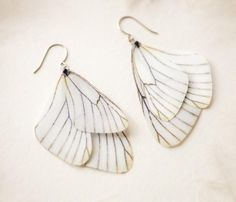 two pairs of white and black leaf shaped earrings on a white tablecloth with silver earwires