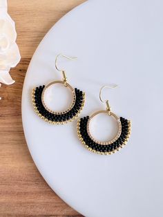 a pair of black and gold hoop earrings sitting on top of a white plate next to a flower