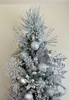 a silver christmas tree with ornaments and snowflakes on it's top, in front of a white wall