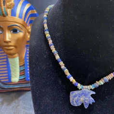 An ancient Egyptian 17 inch long necklace featuring blue and tan disc shaped faience beads and blue glass beads.  Hanging from the faience necklace is a lapis lazuli eye of Horus amulet.  The story of the Eye of Horus came from an epic battle between Seth and Horus in which Horus's eye was shattered into 6 pieces.  Seth was defeated and the eye restored.  Circa 300 to 50 BC Traditional Lapis Lazuli Beaded Necklace, Blue Pendant Beaded Necklace With Single Strand, Blue Amulet Style Hand-strung Necklace, Blue Amulet Necklace, Hand-strung, Blue Handmade Amulet Necklace, Bohemian Single Strand Lapis Lazuli Beaded Necklace, Seth And Horus, The Eye Of Horus, Epic Battle