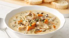 a white bowl filled with chicken and vegetable soup next to sliced bread on a cutting board