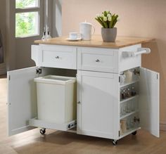 a white kitchen island with two trash cans on it's wheels and a wooden counter top