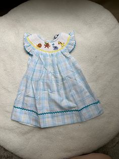 Features: Lovely dress, hand smocked animals around a circle neck, blue zigzag on the sleeves and hem of dress, and short, cap sleeves Perfect for any occasion! Fabric: Blue gingham fabric, blue and yellow accents, cotton, smocking READY TO SHIP! Wash Instructions: machine was on a delicate cycle in cold water to maintain the fabric The clothes will be stiff from shipping so wash them BEFORE you use them. This is important to make sure to remove any additional dye and soften the fabric (no need Gingham Cotton Smocked Dress With Short Sleeves, Playful Cotton Smocked Playtime Dress, Playful Smocked Short Sleeve Dress, Playful Smocked Dress With Short Sleeves And Ruffles, Playful Smocked Dress With Ruffles And Short Sleeves, Fitted Blue Smocked Dress For Playtime, Blue Short Sleeve Smocked Dress With Smocked Cuffs, Playful Smocked Short Sleeve Summer Dress, Playful Smocked Dress With Short Sleeves For Summer