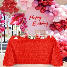 a table topped with balloons and a red table cloth next to a sign that says happy birthday