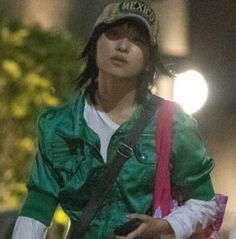 a man with long hair wearing a green jacket and holding a pink bag in his hand