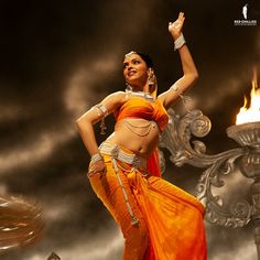 a woman in an orange sari dancing with fire behind her on a cloudy day