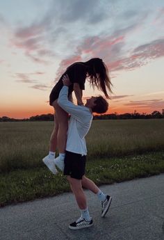 two people standing on top of each other in the middle of a road at sunset