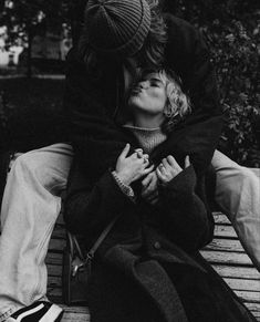 black and white photograph of two people sitting on a bench, one kissing the other