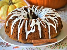 a bundt cake with icing and cinnamon sticks on a plate next to pumpkins