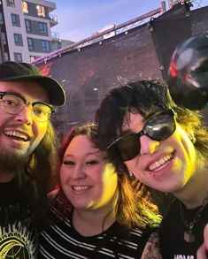 three people posing for a photo in front of a building with neon lights on it