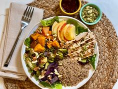 a white plate topped with lots of food next to a fork and bowl filled with fruit