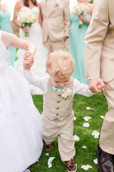 a little boy in a suit and bow tie holding the hand of his bridesmaid