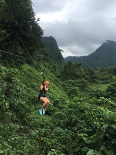 a woman is zipping through the jungle on a rope line with mountains in the background