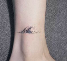 a small wave tattoo on the ankle is shown in black and grey ink, with an ocean wave coming out of it