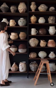 a woman standing in front of a shelf filled with vases