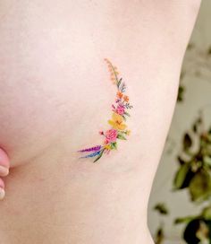 a woman's stomach with colorful flowers on the side and behind her is a tattoo