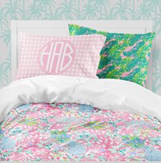 a bed with pink and green floral comforter, two pillows and a monogrammed pillow