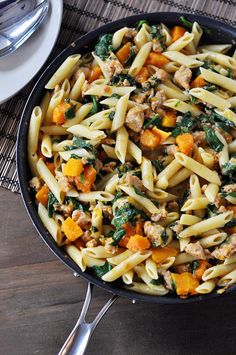 a skillet filled with pasta and vegetables on top of a wooden table