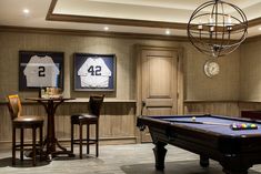 a pool table and stools in a room with baseball jerseys on the wall behind it